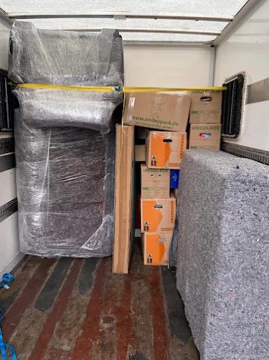Beladener Laderaum mit gestapelten Umzugskartons, einer eingewickelten Couch und einem Spanngurt quer über der Ladung.