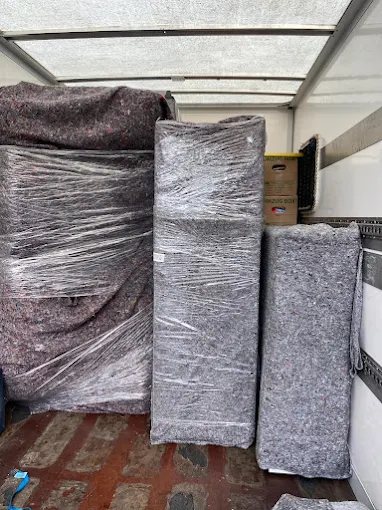 In Umzugsdecken und Stretchfolie eingepackte Möbelstücke stehen aufrecht im Laderaum eines Transporters.